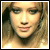 Pixelated close-up of a person's face with light brown hair, neutral expression, and visible eyes nose mouth against blurred background.