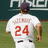 A pixelated image of a baseball player in a white uniform with red number 24 on the back, standing on a field with a blue showing red text and numbers