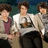 Animated sequence of a person in a white sweater with a graphic, dark pants, and maroon undershirt, seated in a with others against a blue background