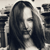 A grayscale pixelated image of a person with long hair, partially obscured by a blurred background with vertical and horizontal shapes.