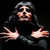Pixelated image of a person with long dark hair and glasses, wearing black clothing, extending both hands forward against a solid black background.