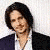 A person with long dark hair wears a white shirt and dark jacket, holding up blue jeans while smiling; partial text 'Damn.' appears below.