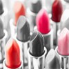 Multiple lipstick tubes with open caps showing various colored lipsticks in shades of red, pink, and orange against a blurred background.