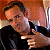 Pixelated image of a person in a black shirt holding a microphone, with a blurred background showing warm tones and a vertical light source.