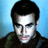 Pixelated static image of a person with dark hair and light skin against a blue background, wearing a dark jacket.