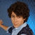 A person with curly brown hair in a dark jacket and light shirt poses against a blue background, shifting expression from neutral to smiling.