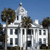 Pixelated image of a white building with columns, a domed tower, and trees against a blue sky.