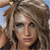 A pixelated close-up of a person with light brown hair styled in a high ponytail, wearing dark clothing against a blurred outdoor background.