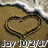 A heart shape drawn in sand with a small black dot inside, waves crashing on the shore behind it.