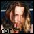Pixelated close-up of a person with light brown hair and fair skin, wearing dark clothing against a blurred background with visible text "FAN" at the bottom left.
