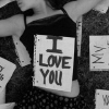 Black-and-white image of a small rectangular sign with bold text "I LOVE YOU" held against a patterned background.