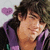 Pixelated image of a person with dark hair wearing purple clothing, holding hand near face, with pink heart symbol in background.