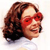 Pixelated close-up of a person with brown curly hair wearing red sunglasses and a white top against a light background.