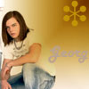 A person with shoulder-length brown hair wearing a white t-shirt and light blue jeans sits against a gradient background with a yellow star-like symbol and partial text.