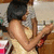A woman with short dark hair in a light-colored sleeveless dress holds her right arm bent across her chest, left hand near her face.