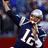 A pixelated image of a football player in a dark blue jersey with white number 12, holding a ball and raising an arm, surrounded by red background with blue text