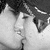 Black-and-white photo of two people kissing, white skull with crossbones on black background, circular badge reading 'Kiss Me I'm EMO' with red lips icon.