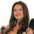 A pixelated portrait of a person with long dark hair, closed eyes, and a slight smile, wearing a dark top with visible straps.