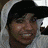 A static image of a person in a gray hoodie with dark hair, wearing a white shirt with text and symbols.
