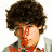 A pixelated image of a person with curly brown hair wearing a light gray jacket over a white shirt, featuring red text overlays on the face and chest.