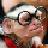 Pixelated static image of a person with light skin tone wearing dark sunglasses and a white cap, holding an object near their face.