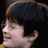Pixelated static image of a character's face with dark hair and light skin, wearing a large dark hat with brown trim against a black background.