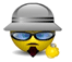 Animated yellow emoji with gray helmet, blue sunglasses, dark red goatee, and small golden bell; mouth changes from downturned to smiling while holding the bell.