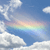 A static pixelated image shows a blue sky with white clouds and a faint rainbow arc across the center.