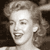 Static grayscale pixel art of a smiling woman with styled hair, cropped to show upper face and shoulders against dark background.