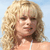 Pixelated image of a person with voluminous blonde curly hair against a light blue background, wearing a white strap top.