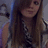 A pixelated static image shows a person with long brown hair wearing a dark top, standing against an indistinct background.