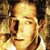 Pixelated close-up of a person's face with light skin tone, dark hair, and a neutral expression against a blurred background.