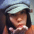 A pixelated image shows a person with dark hair and light skin wearing a white cap, blowing air kisses against an orange background with text.