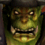 Green-skinned humanoid face with glowing eyes, bared teeth, and dark hair against a dim background.