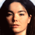 Pixelated close-up of a person's face with dark hair, light skin, and closed eyes, set against a dark background.