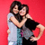 Two people embrace against a solid red background; one wears light clothing, the other dark.