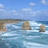 A coastal scene with three rock formations in the ocean, waves crashing against them under a partly cloudy sky.