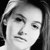 Black-and-white pixelated image of a person's face with light hair, neutral expression, and visible eyes, nose, and mouth against a dark background.