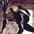 Pixelated image of two figures in a close embrace, one figure in dark clothing with a light-colored head, the other in light-colored clothing with dark hair, against a blurred background.