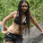 A woman in a black bikini top and black shorts poses with hands on hips against a grassy background.