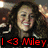A woman with long dark hair smiles while raising her right hand, overlaid with red text reading "I <3 Miley" on a black background.