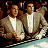 A 2x2 contact sheet of a pixelated animated icon featuring two men in suits at a card table with text overlays, displayed on a gray background.