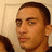 A pixelated close-up of a person's face with short dark hair, light skin tone, and neutral expression against a beige background.