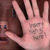 A hand with handwritten text on the palm, held up against a blurred background featuring a person and objects.