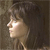 Pixelated profile view of a person with dark hair against a muted brown background, showing partial facial features and neck.