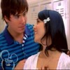 Two people in close proximity, one wearing a blue striped polo shirt with a white collar and a white bow in dark hair, the other in a white top with a low neckline.