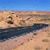 Pixelated landscape with blue sky, sandy terrain, and dark water body, rendered in low-resolution style.