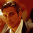 Pixelated static image of a man's face with brown hair and light skin, wearing a white shirt against a red background.