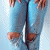 Pixelated image of a person wearing blue jeans and brown shoes, standing against light blue background with white pixel clusters.