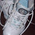 A pair of white sneakers with light blue accents and laces, shown in two states: one with a metallic gold sole visible and another without.